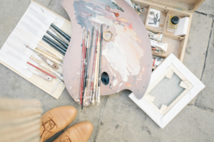 A picture of a pile of pretty art supplies outside, on the ground arranged around the artists feet.