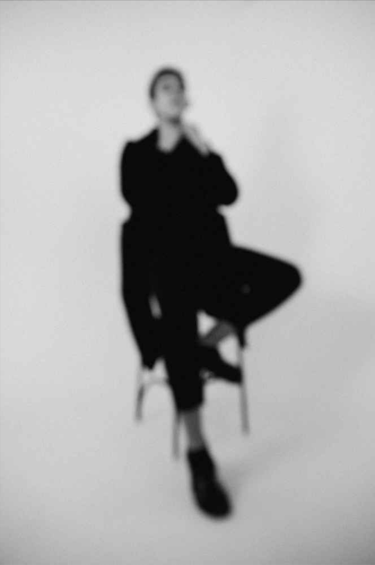A blurry image of a person seated in a studio.